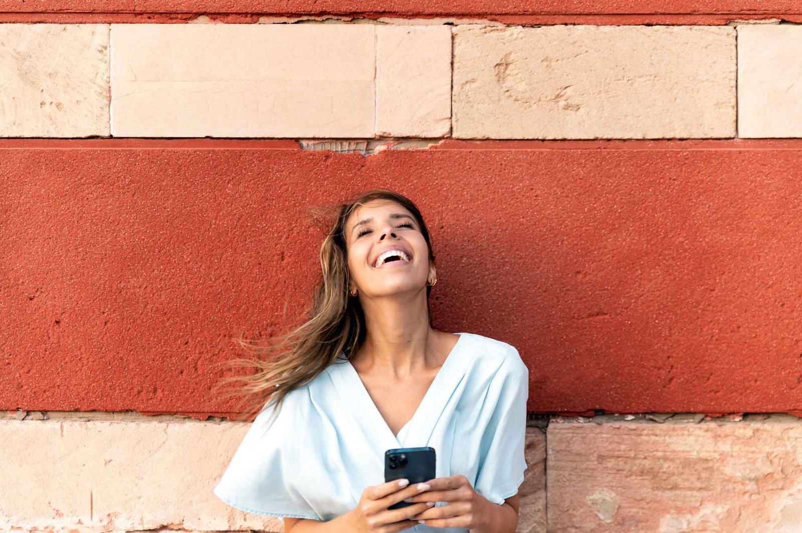 Mulher bonita sorrindo com seus cabelos esvoaçantes e segurando o seu celular.